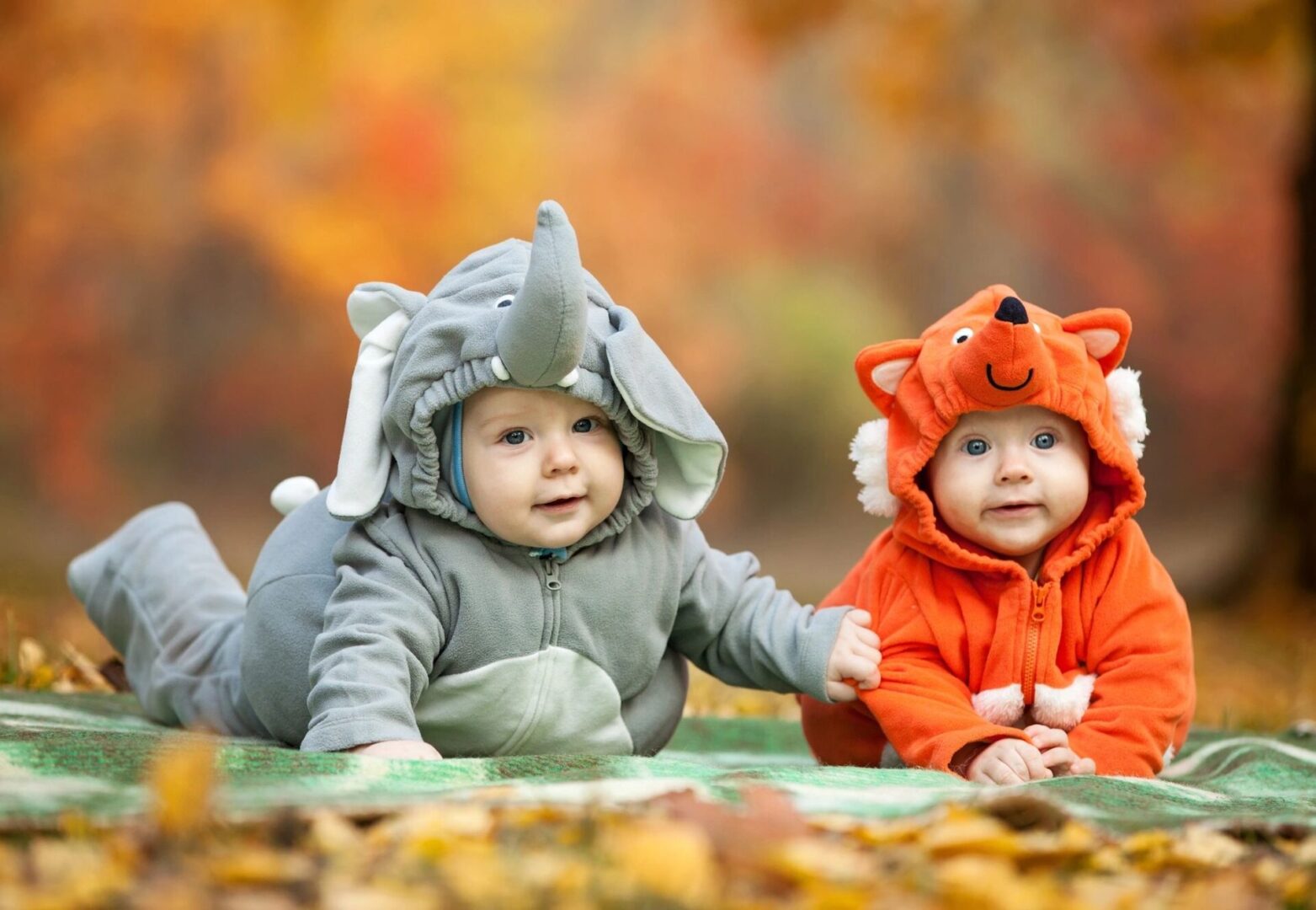 Two babies dressed in costumes sitting on the ground.