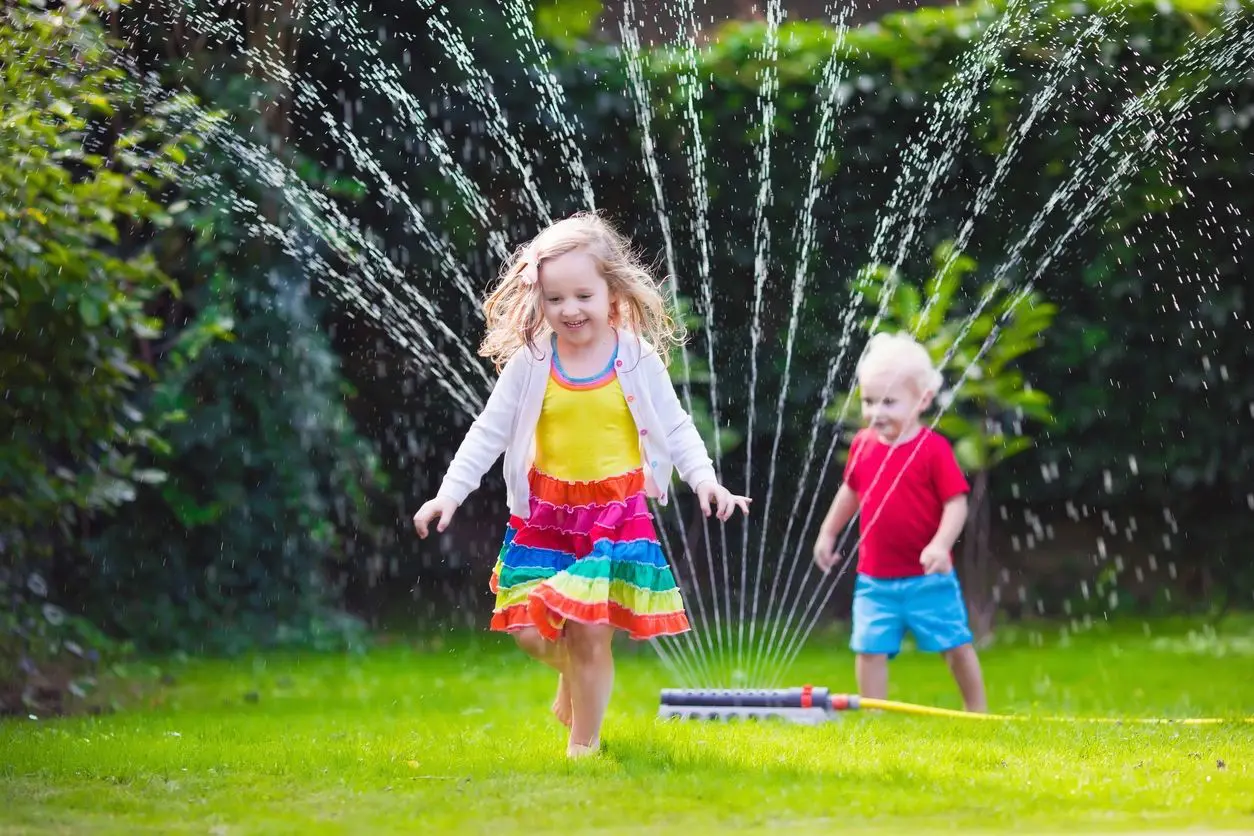A young girl and boy playing with sprinklers in the yard.
