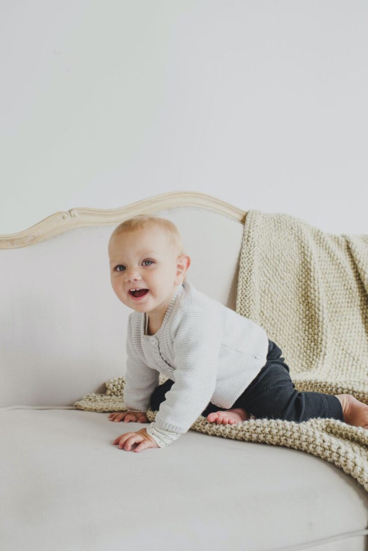 A baby is smiling while sitting on the bed.